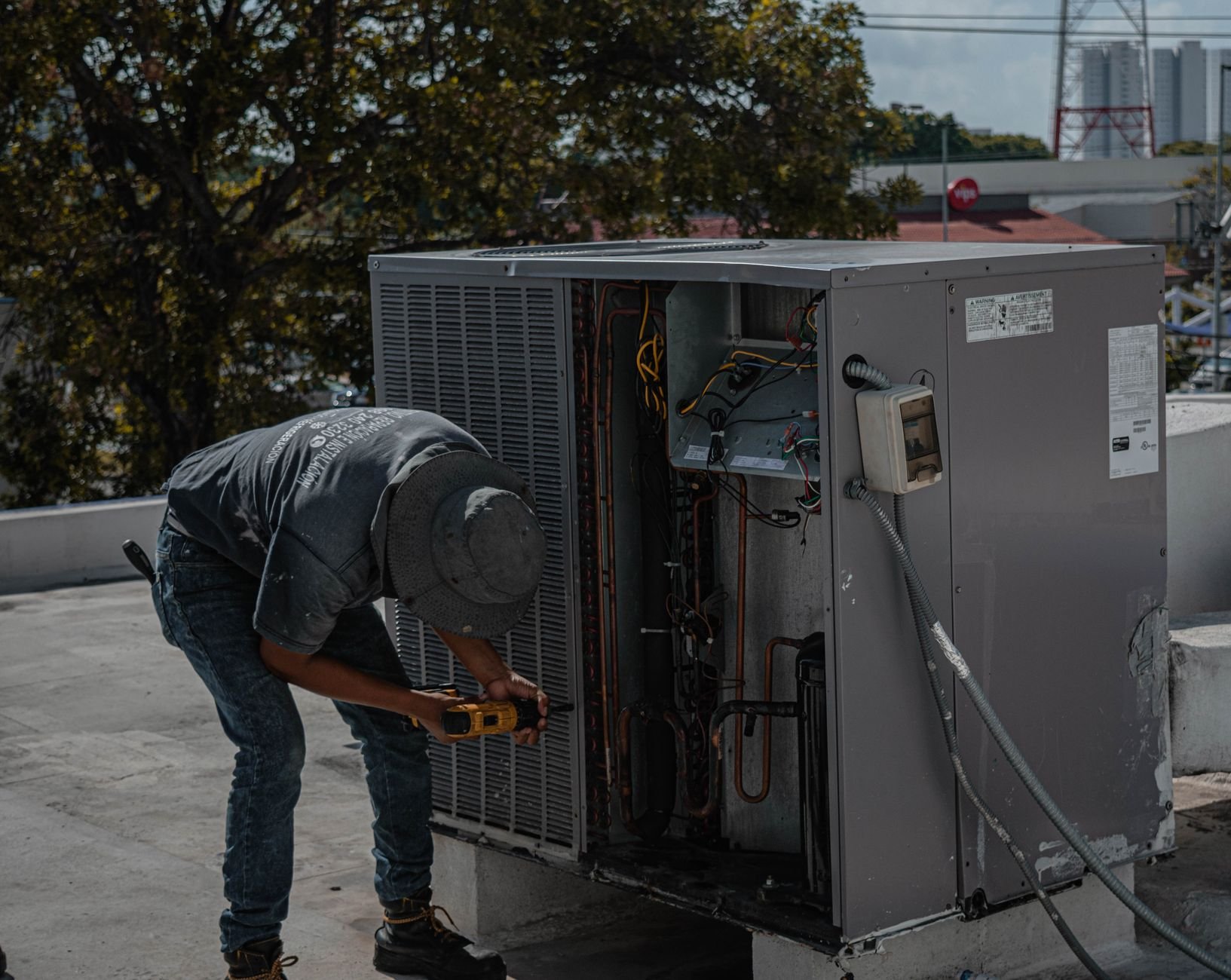 A technician repairing an air conditioning unit on a rooftop, demonstrating skilled manual work.
